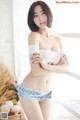 A woman in a white top and blue shorts posing by a window.
