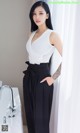 A woman in a white top and black pants posing for a picture.